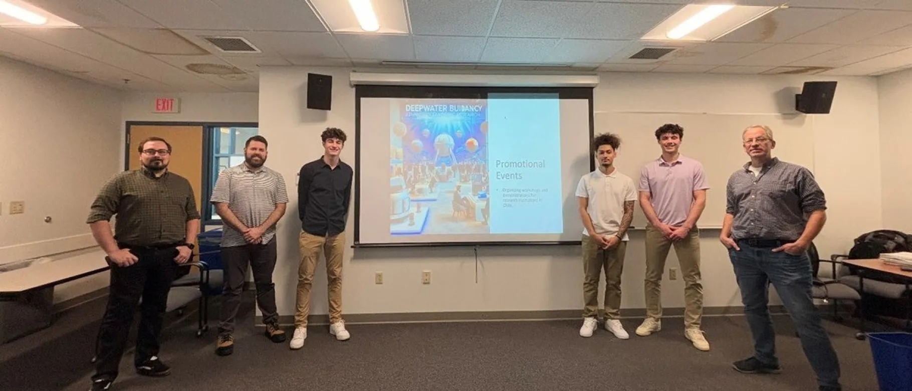 UNE students pose in front of a slideshow presentation with members of the DeepWater Buoyancy sales team