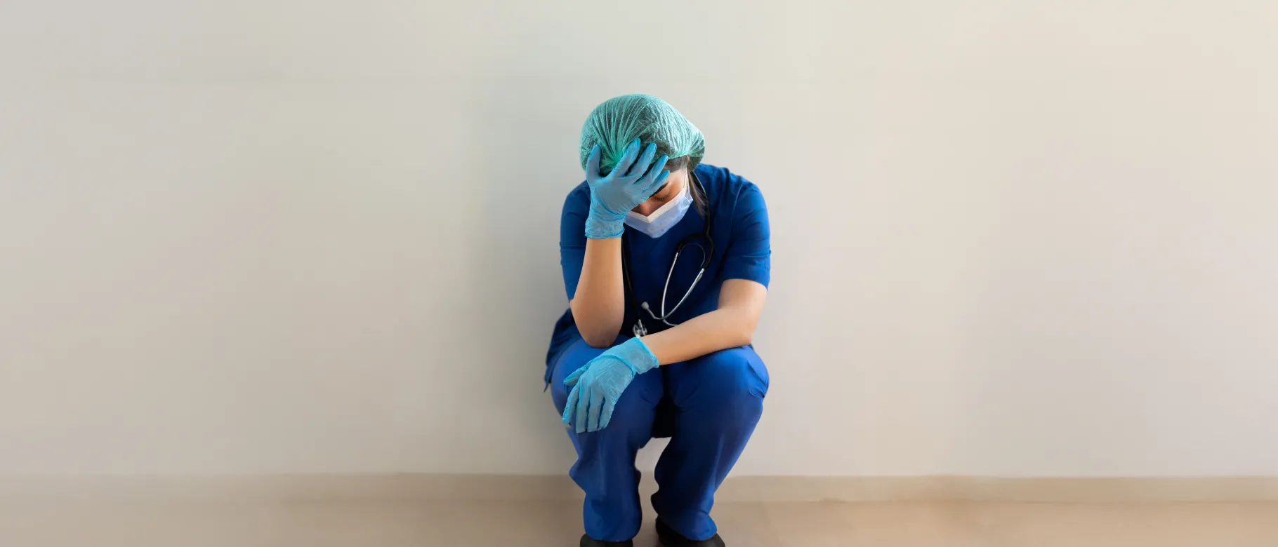 An image of a health worker in scrubs holding their head in disbelief 