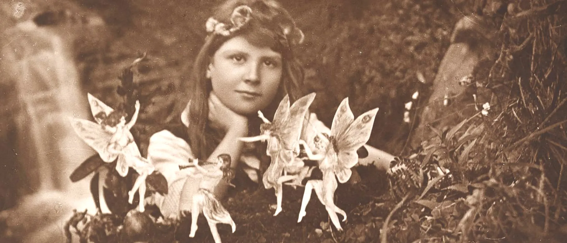 Sepia image of a girl in the woods surrounded by fairies