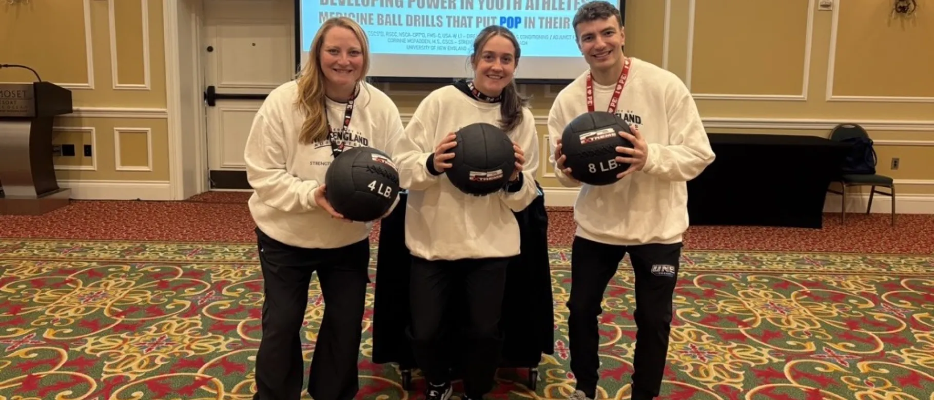 UNE student Aidan Curran poses with his research collaborators, all three are holding medicine balls