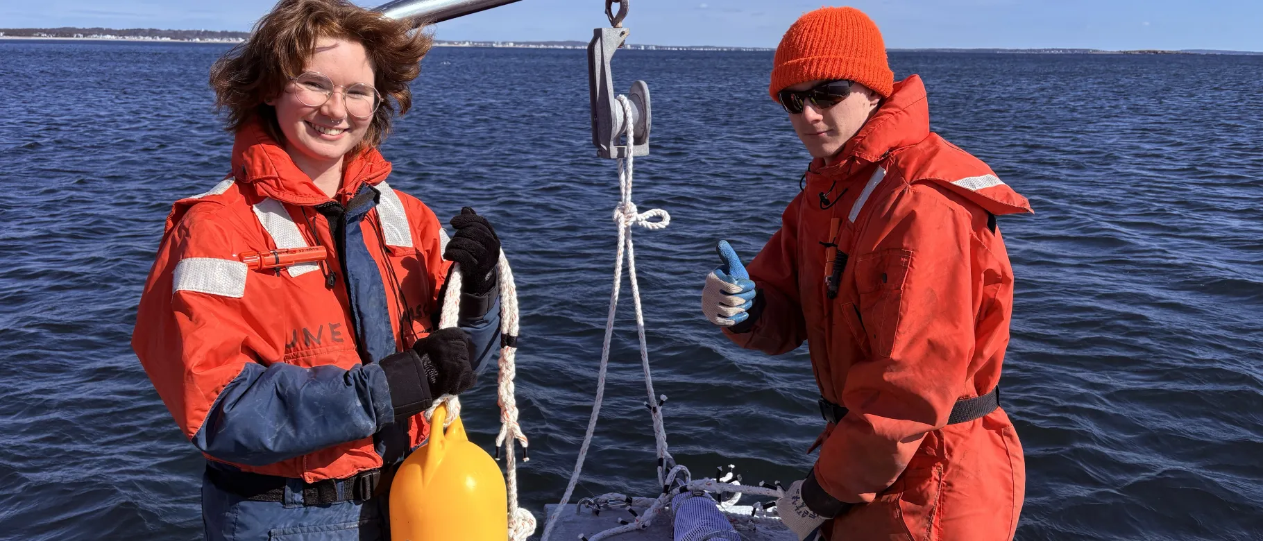 Two UNE students pose with a wave monitoring device on a research boat
