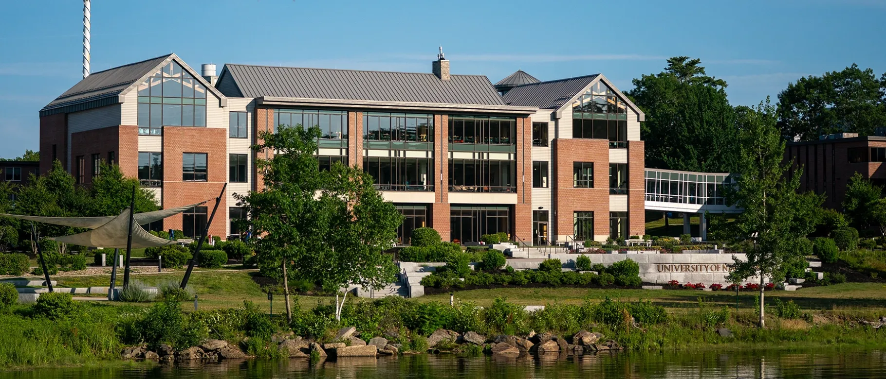 The Commons building at U N E's Biddeford Campus, reflected in the water at golden hour on a summer evening.