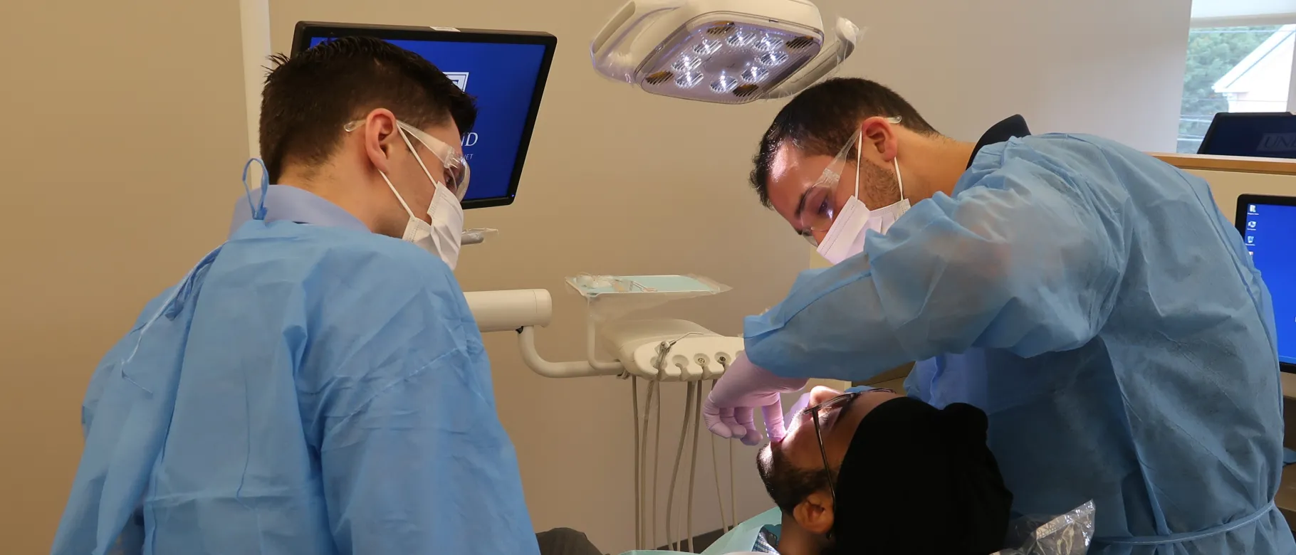 COM student Govind Kamboj plays a patient while CDM student Greg Stein explains a procedure to COM student Ryan Healy