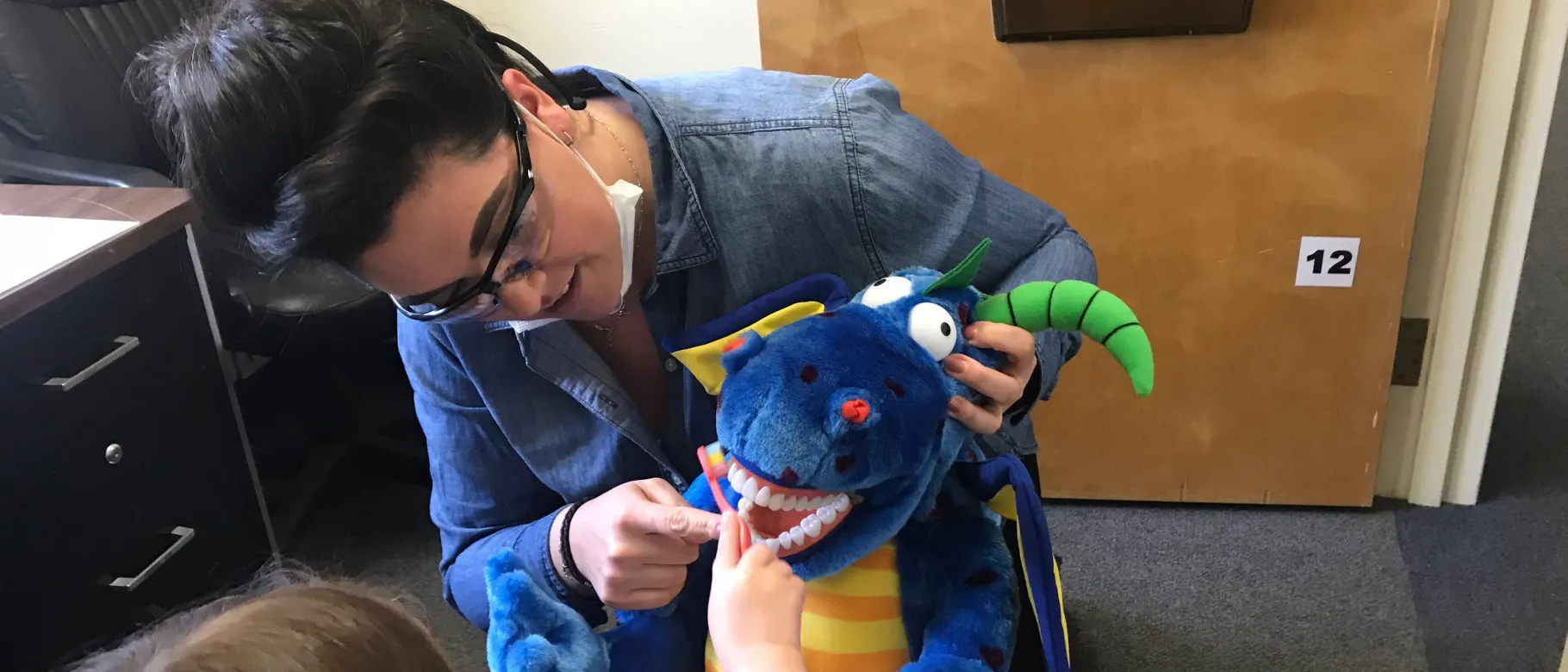 Dental student Ayla Nelson helps a young patient practice her toothbrushing skills using a stuffed animal