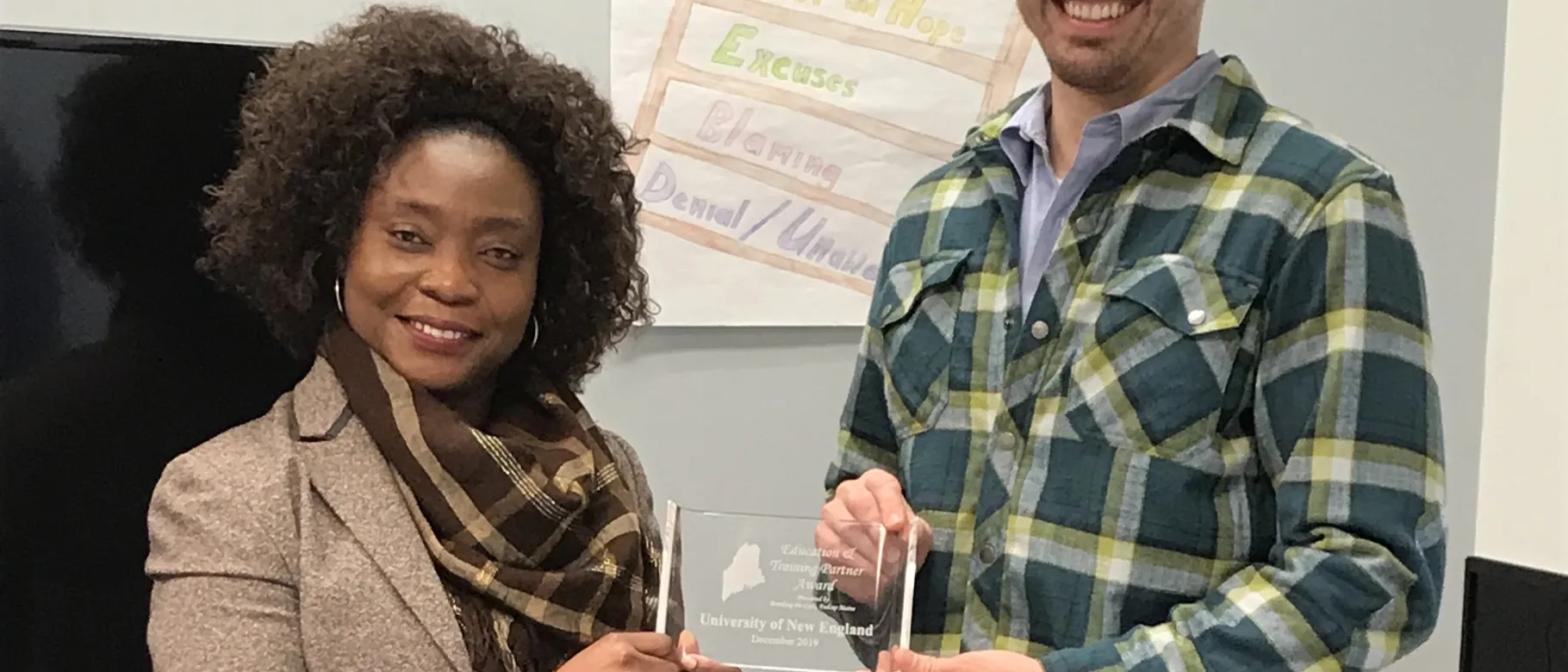 FedCap Biddeford Site Manager Sianeh Omeze presents UNE with the Education Partner Award, accepted by Ian Imbert, M.P.H.