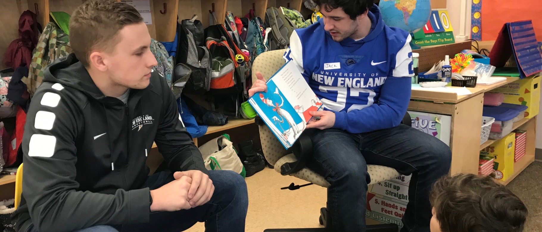 UNE student-teacher Drew Patno looks on as football player Jack Mahoney reads to children at the Eight Corners School