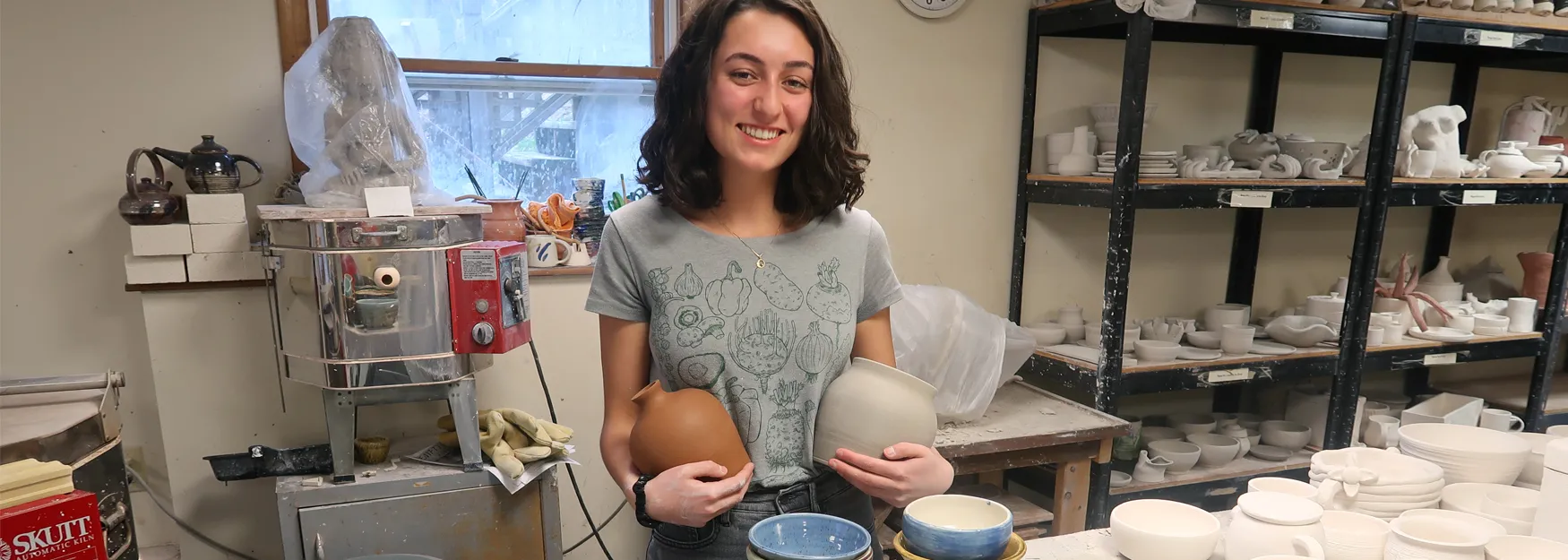 Olivia Scott stands smiling at the camera holding her handmade ceramics