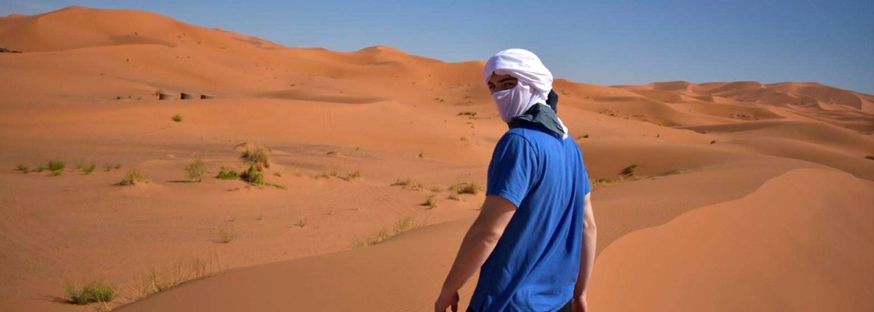 Devin Jozokos stands among the Sahara Desert, turned back to look at the camera