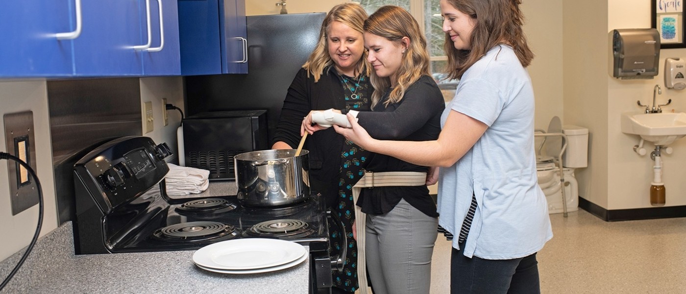 Students help a patient with an inured wrist stir a pot on the stove