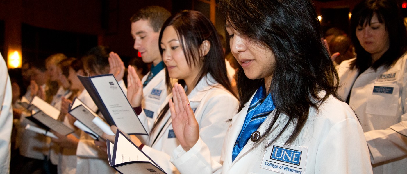 First-year pharmacy students stand in their white coats and recite the pledge of professionalism 