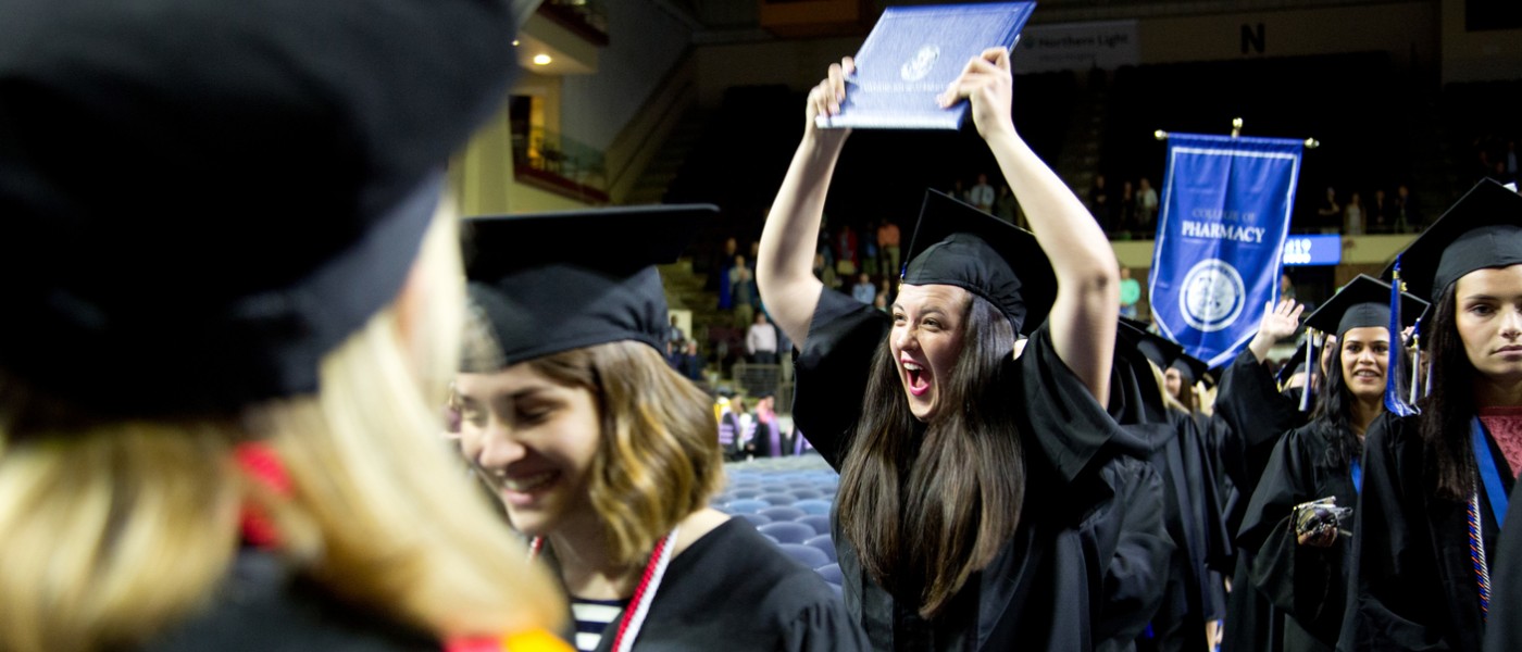 A female student holds her diploma over her head in celebration at commencement