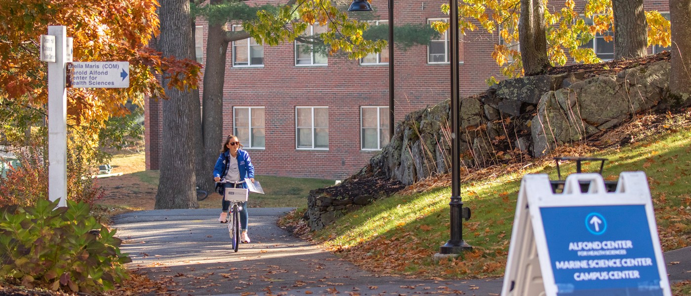 a student rides a bicycle through the biddeford campus in the fall