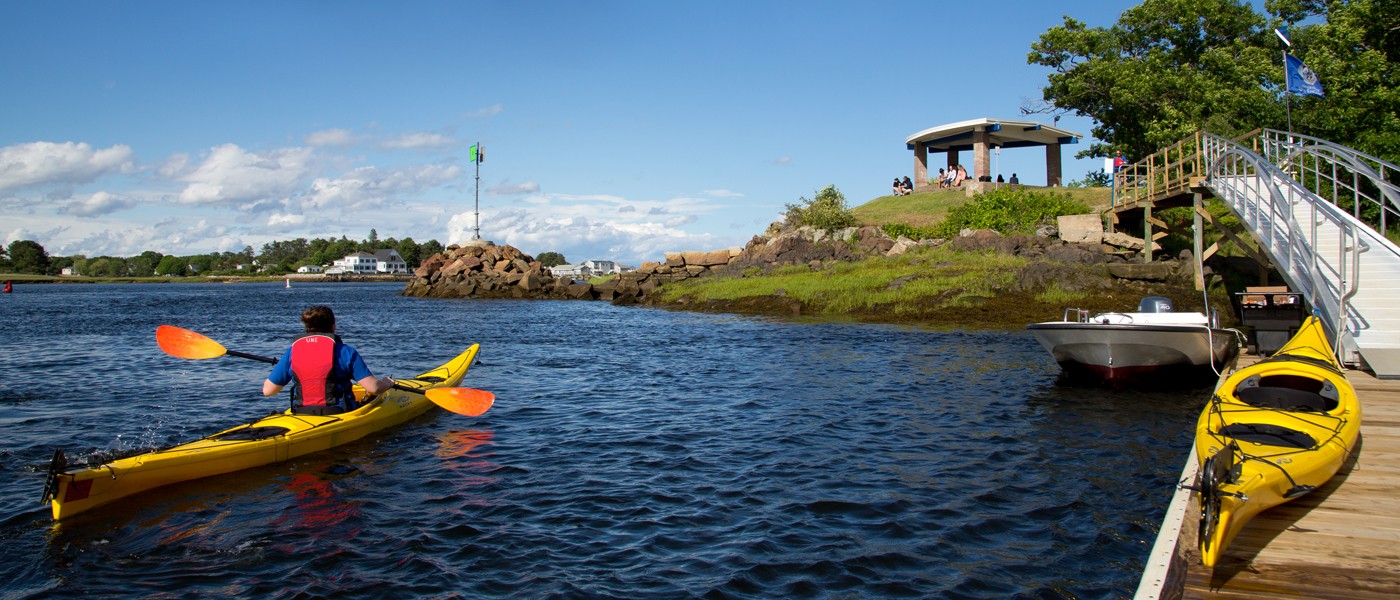 a student paddles a kayak on the ocean along the shoreline of U N E's biddeford campus