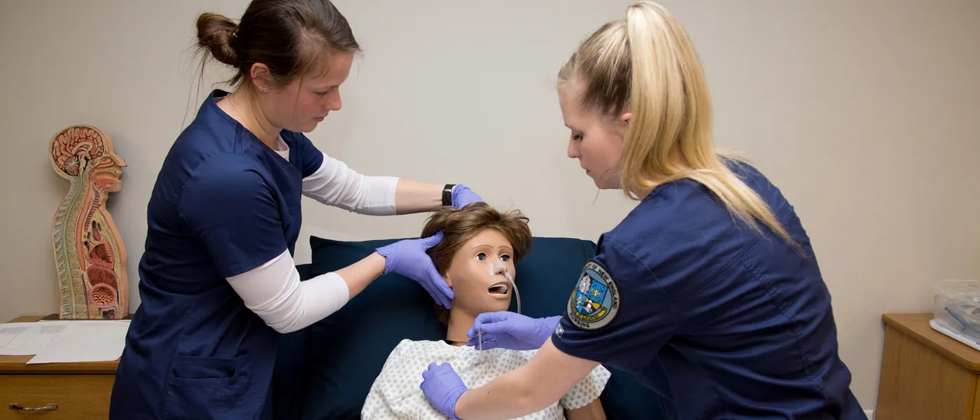 Two female students practice on a patient simulator