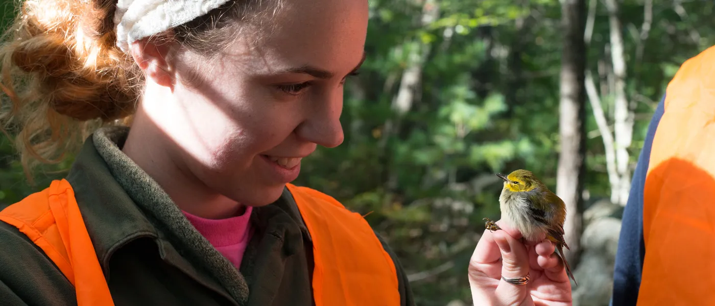 A female student looks at a small bird perched on her hand