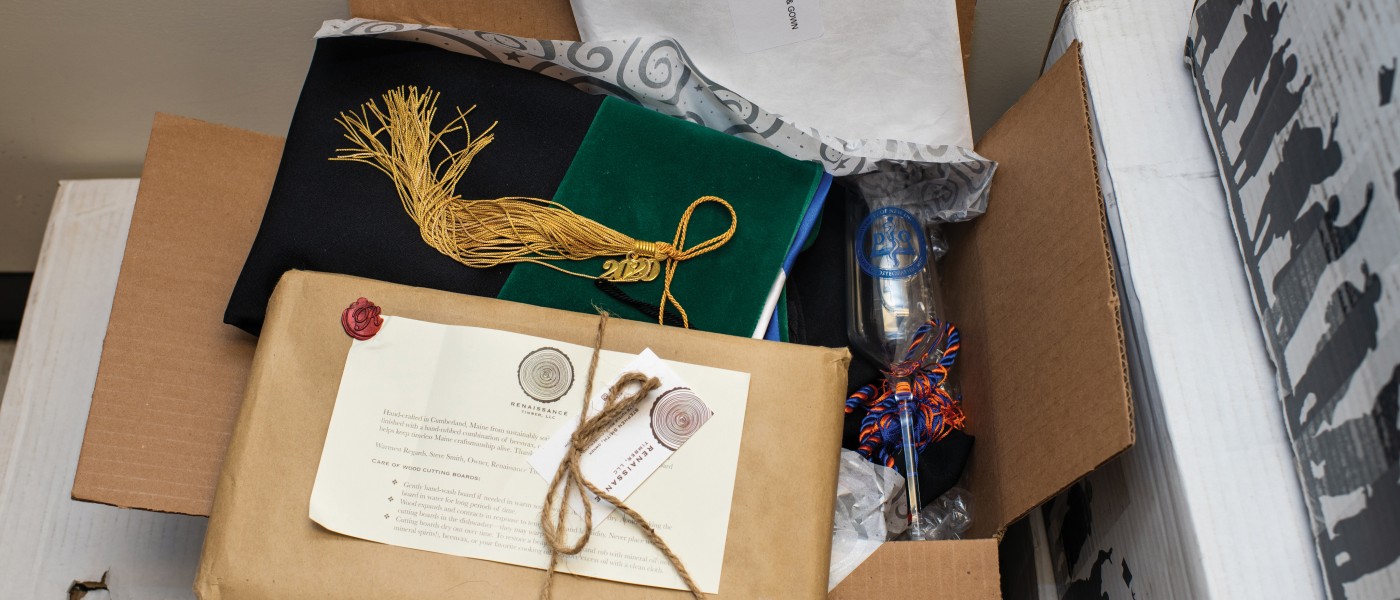 An overflowing package of COM Commencement materials, including caps, gowns, and a customized champagne flute.