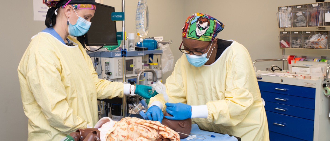 A U N E health professions student wearing scrubs works on a patient simulator