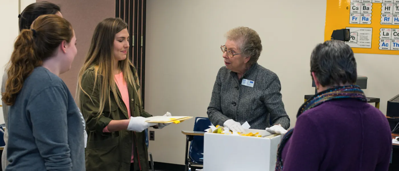 Three U N E liberal arts students discussing documents with two professors
