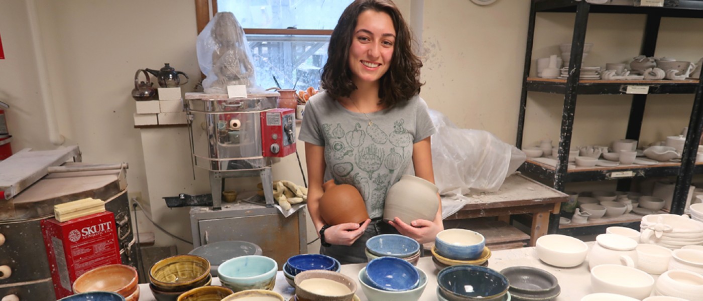 A U N E liberal arts student stands in front of a display of pottery she made in an arts class
