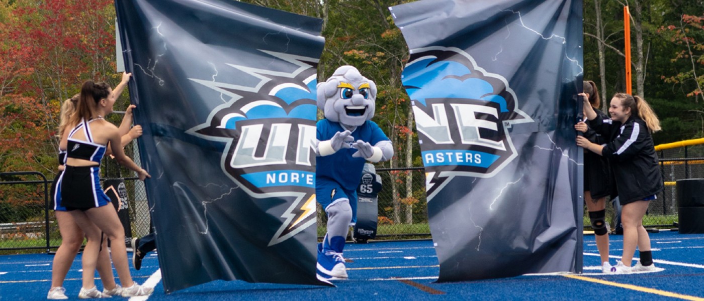 U N E mascot Stormin' Norman running through a banner at a football game