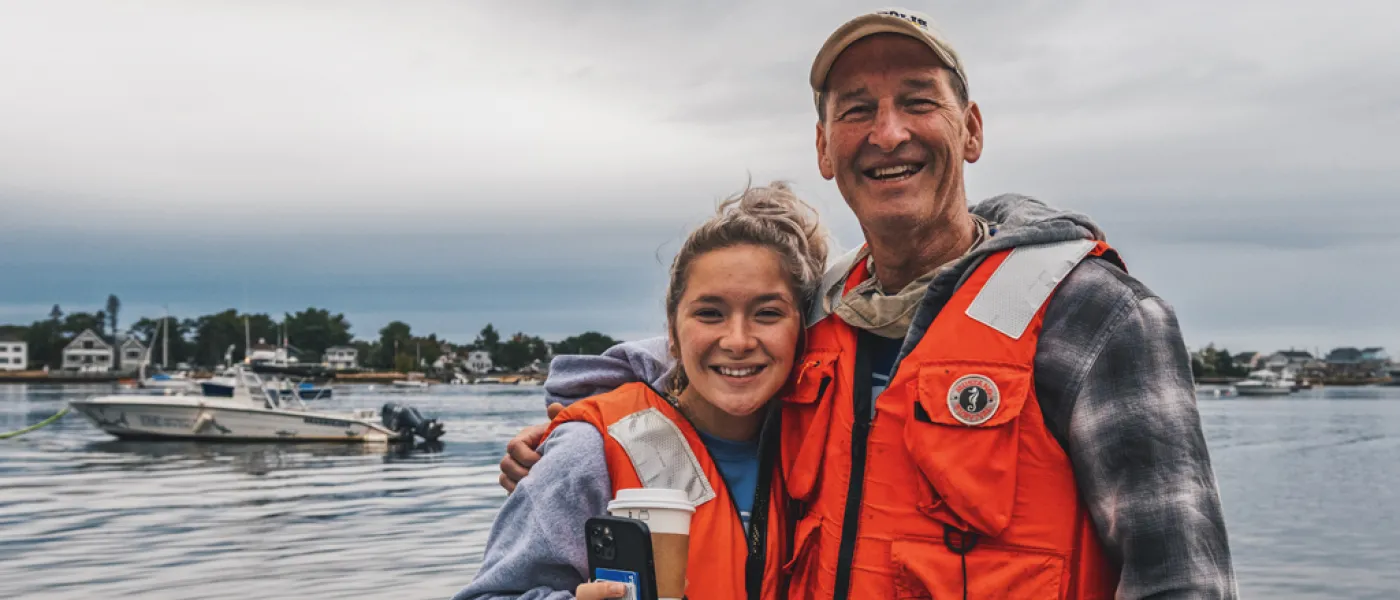 Parent and U N E student in life jackets by the water