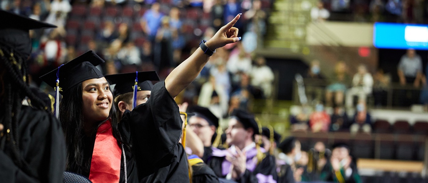 A graduate points to friends from the arena floor