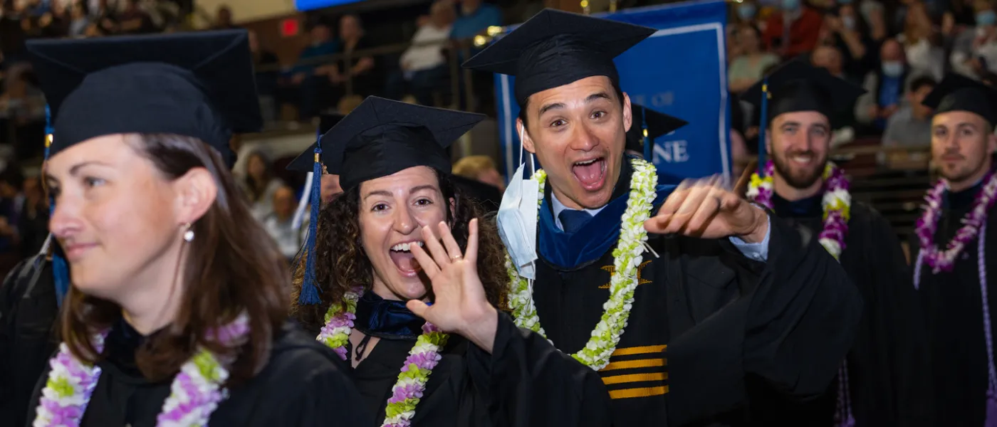 Two graduating U N E students smiling and waving excitedly