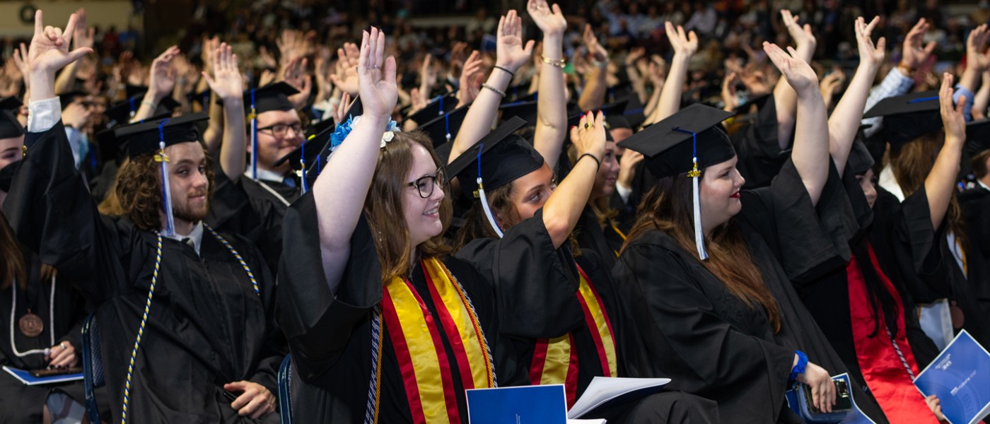 Graduating U N E students raising their hands in the air