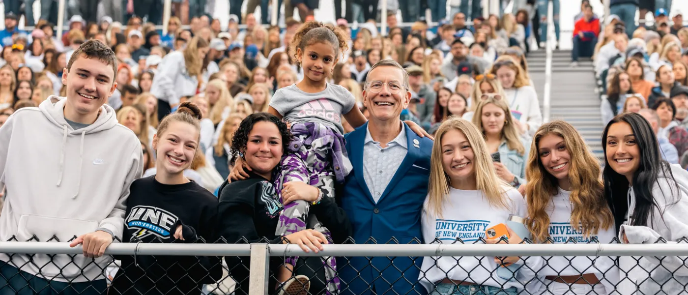 Students stand with President Herbert at a U N E football game