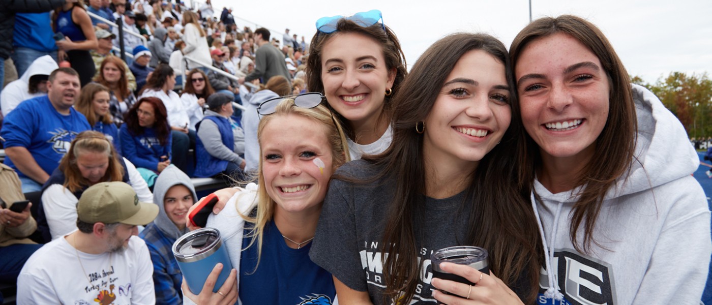 Several students at a U N E football game smile at the camera