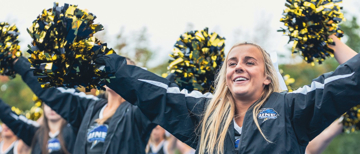 Close-up of a U N E cheerleader with their pom poms