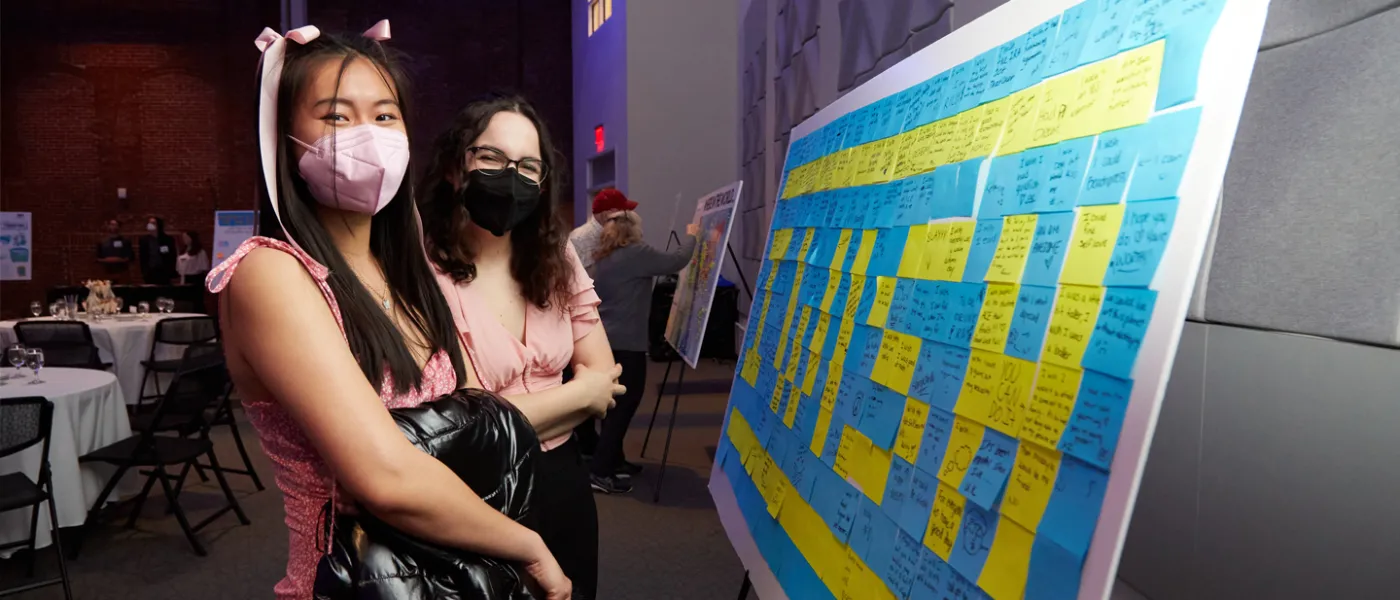 Two U N E students looking at a post-it note art piece
