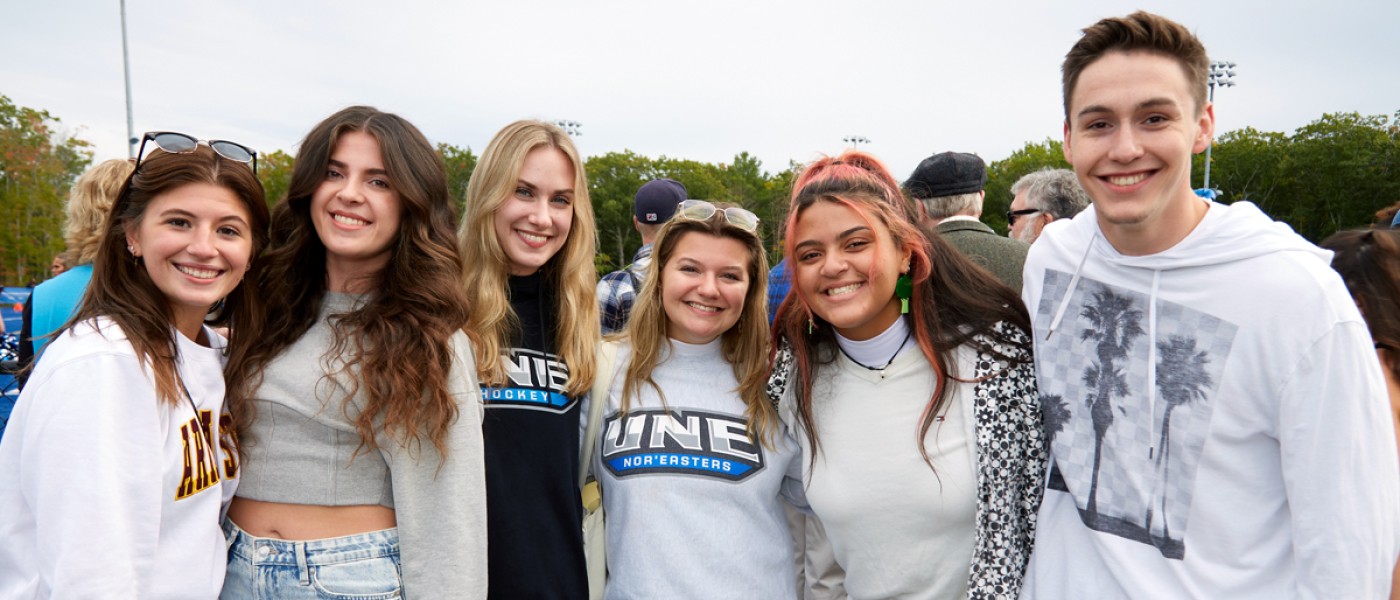 Several students standing together at a U N E Homecoming football game