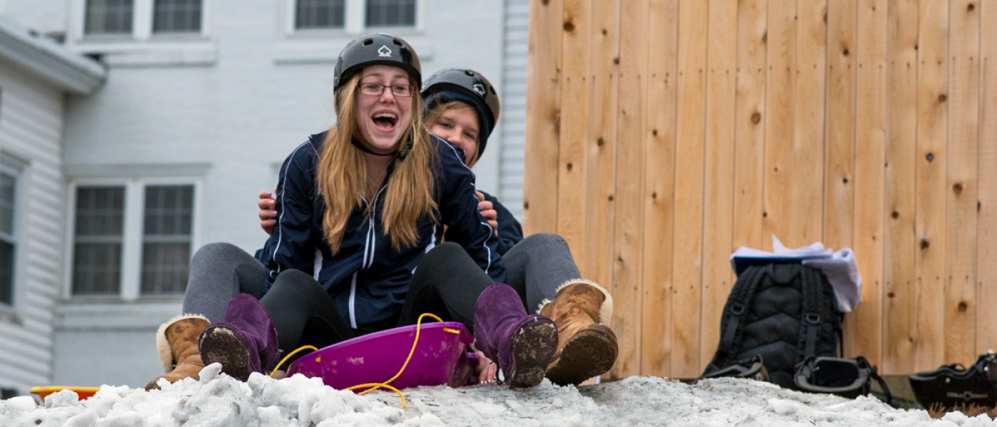 Two students about to sled down a small hill on the Biddeford Campus