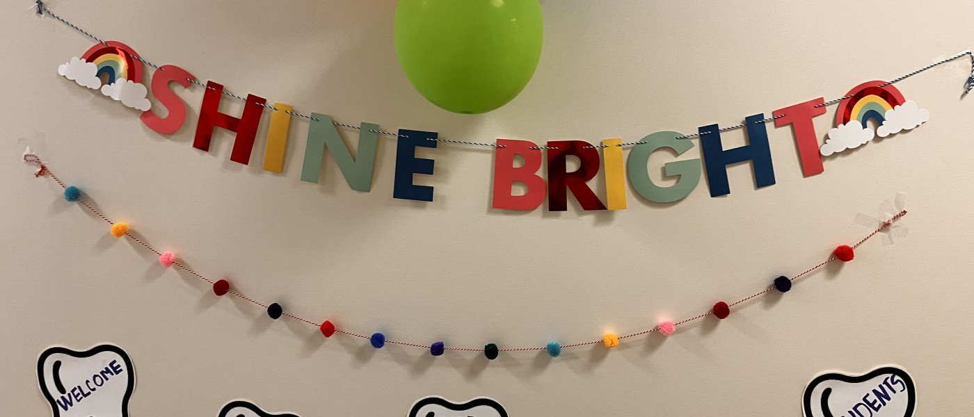 A sign saying "Shine Bright" is displayed, along with balloons and tooth-shaped cutouts that individually spell out "Give Kids a Smile"