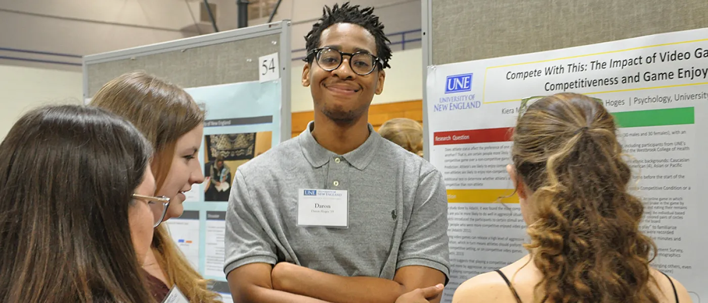 A student speaks about their poster presentation to three people