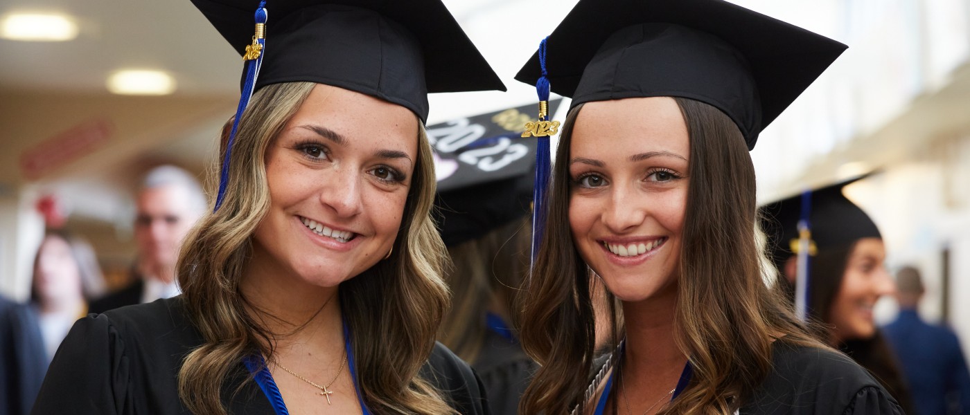 Two students wearing cap and gown pose at U N E's 2023 commencement ceremony