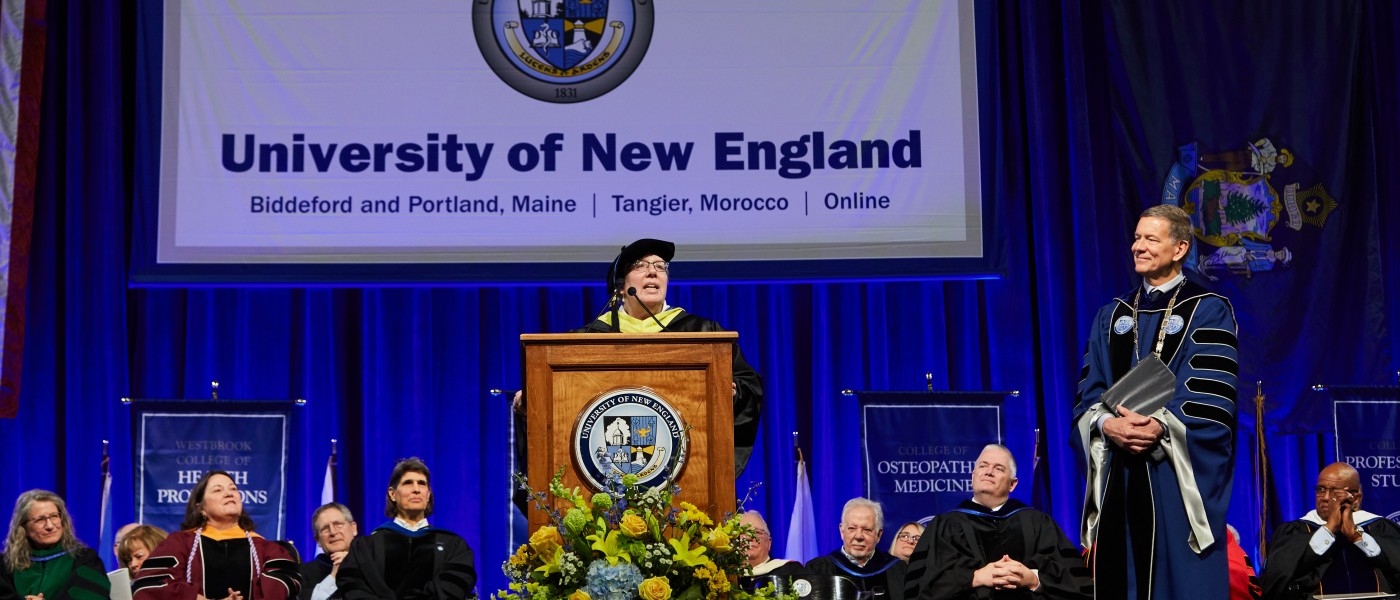 a faculty member speaks at the podium while other faculty and the university president look on at 2023 commencement