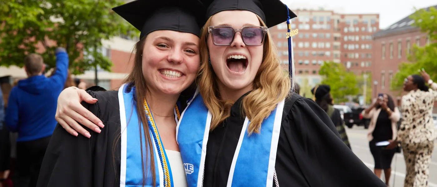 U N E Students dressed in cap and gown pose outside the 2023 commencement venue