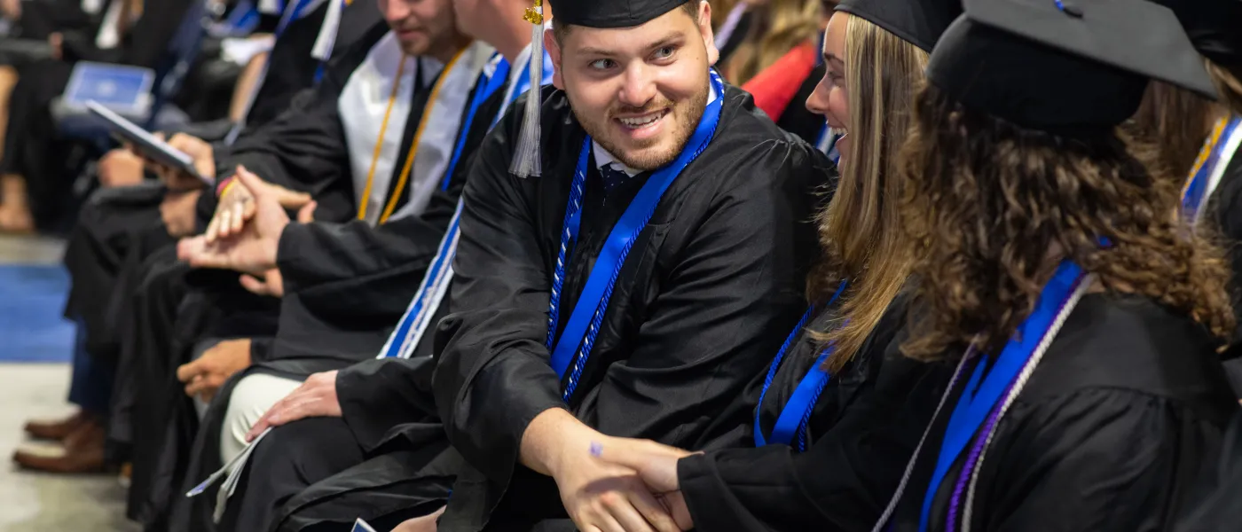 Students dressed in cap and gown sit in rows at U N E's 2023 commencement ceremony