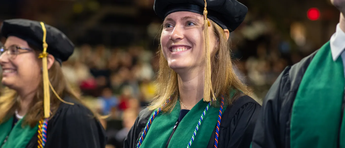 A student stands in the crowd in cap and gown at the 2023 U N E commencement ceremony