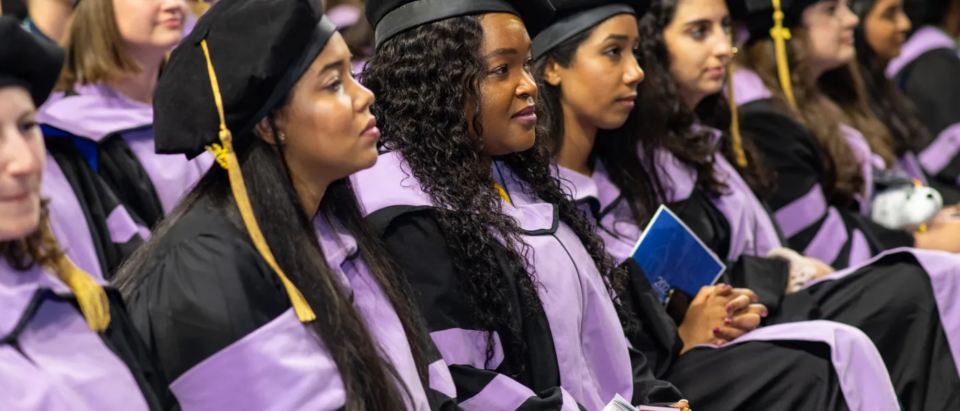 Students wearing cap and gown sit in a row at the 2023 UNE Commencement ceremony