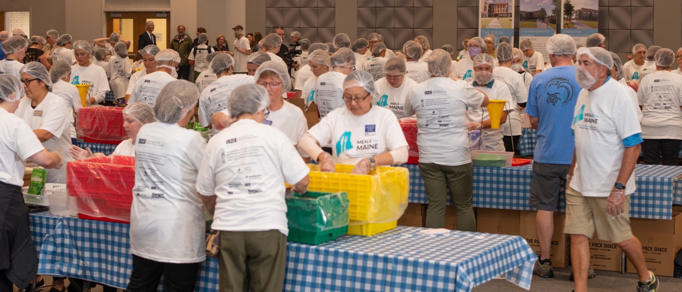 A room filled with Meals for Maine volunteers working to pack meals