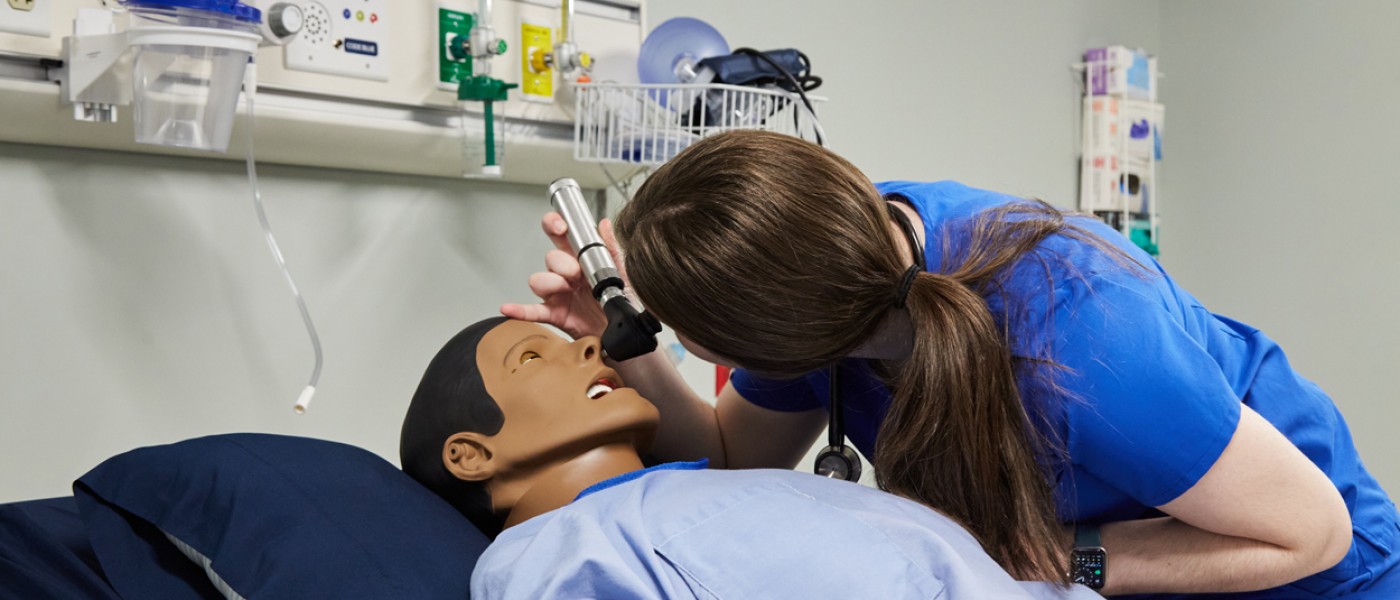 A physician assistant student uses an otoscope on a patient simulator