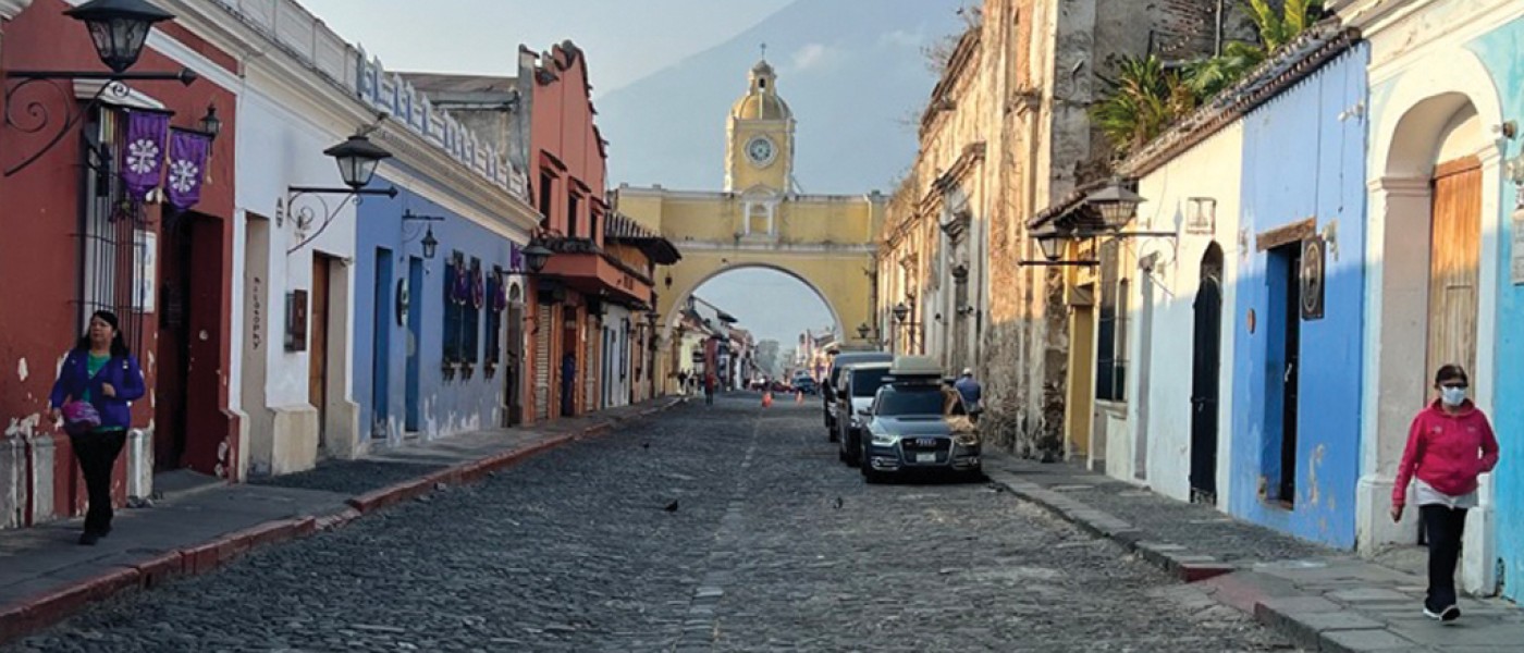 Street view of colorful buildings that lead to a yellow arch with a tower