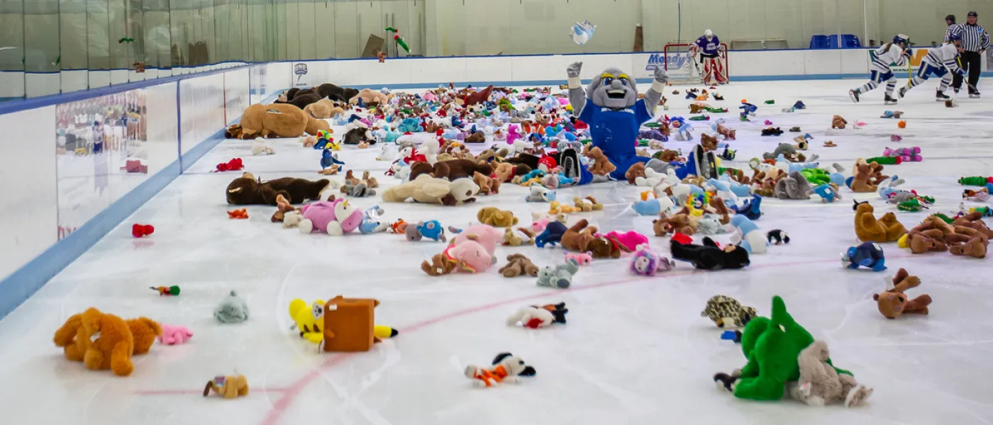 U N E mascot Stormin' Norman sits on the ice of a honkey rink surrounded by stuffed animals for a Teddy Bear Toss event
