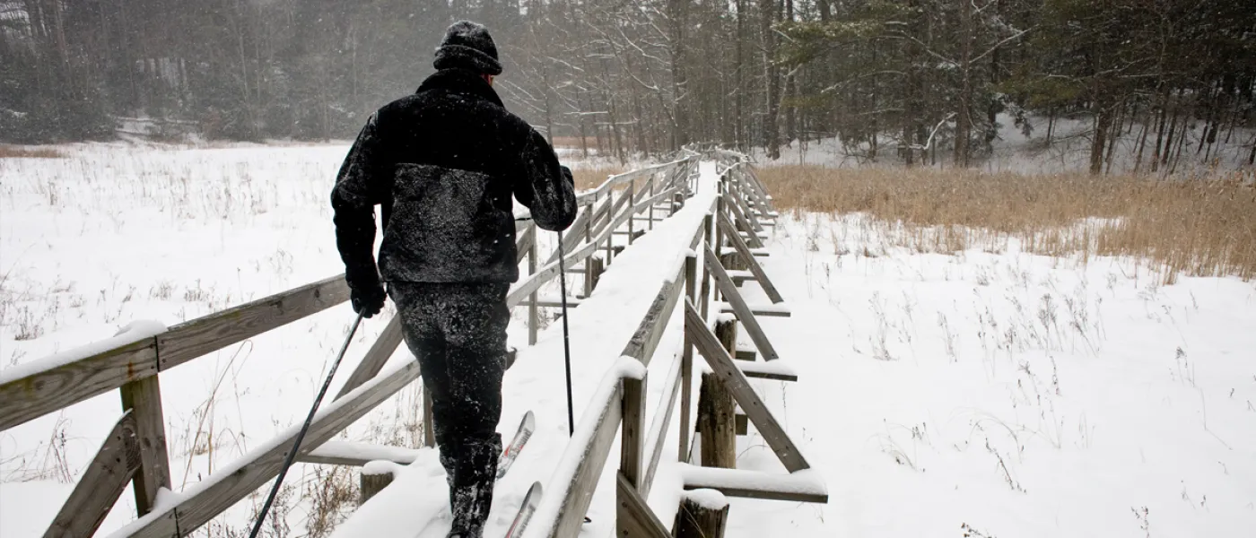 A man cross-country skis over a snow-covered bridge