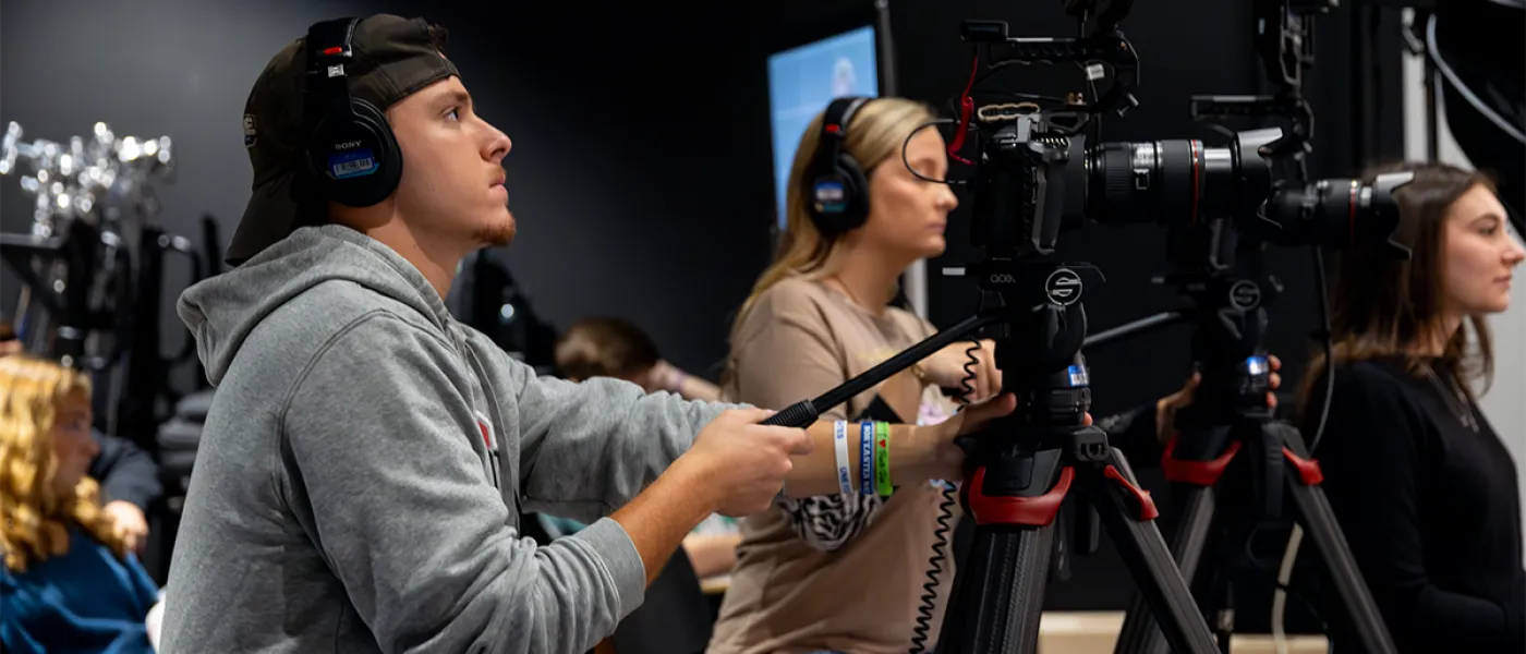 A student works a video camera during a mock interview for a communications class