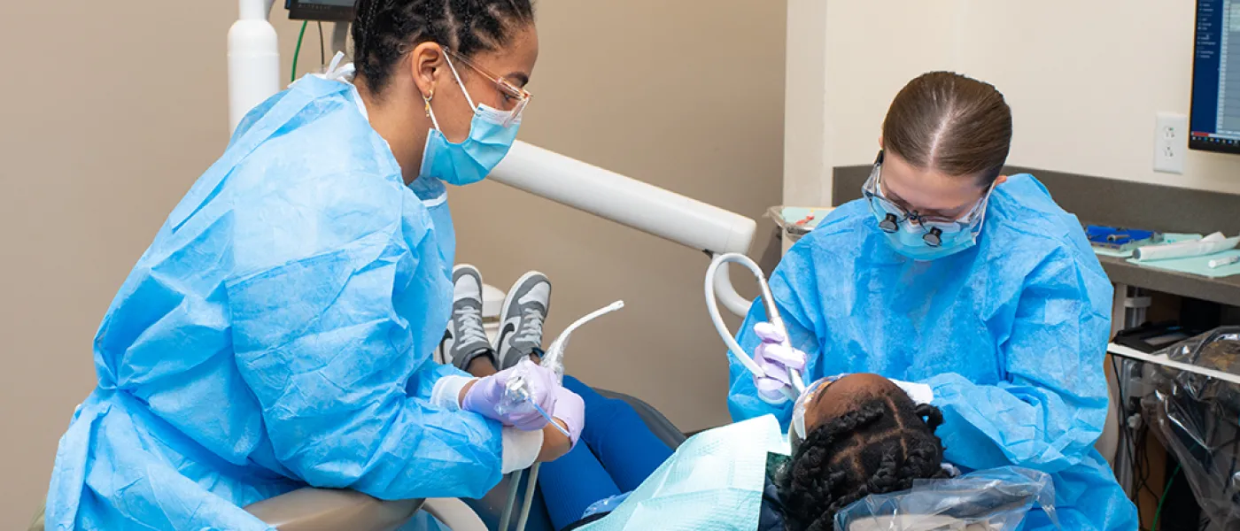 Two C D M students work together to clean the teeth of a child in the Oral Health Center