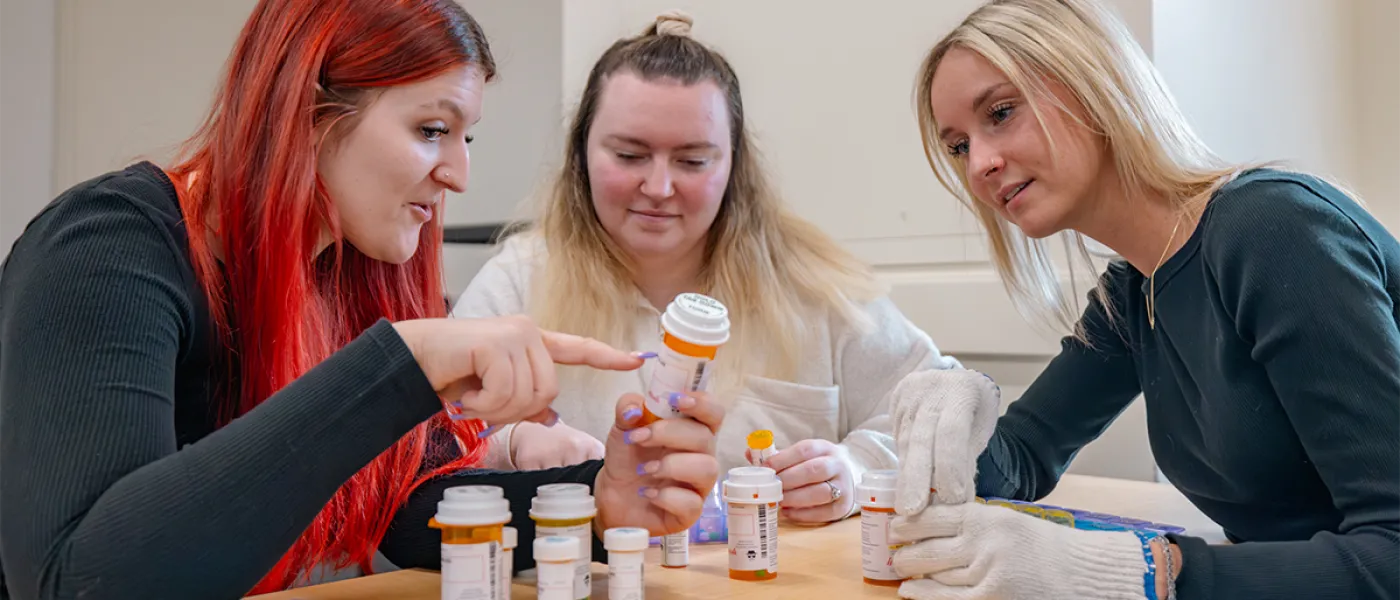 Three students review bottles of prescription medication in a classroom setting